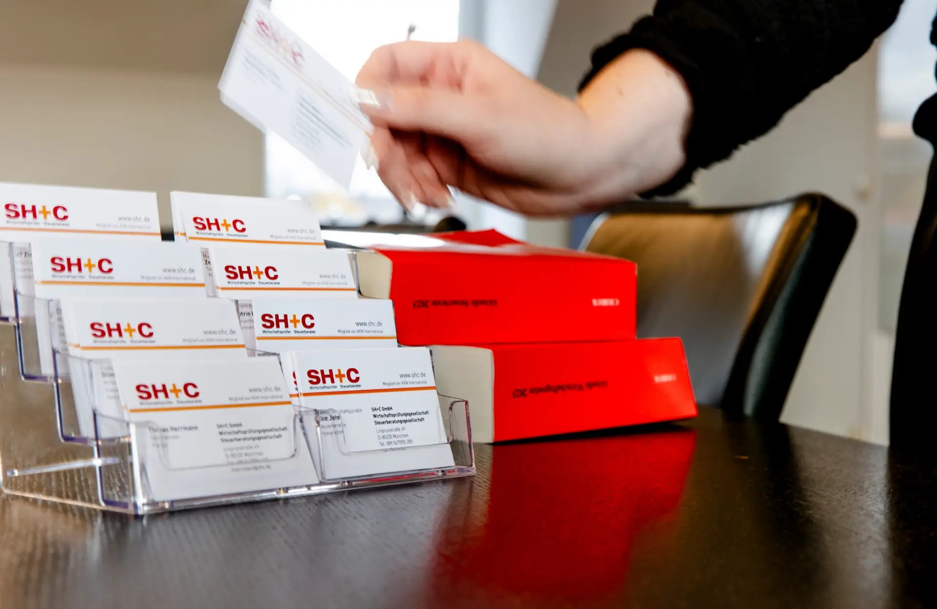 Visitenkarten von SH+C in rot-orangenfarbenem CI im transparenten Visitenkartenständer