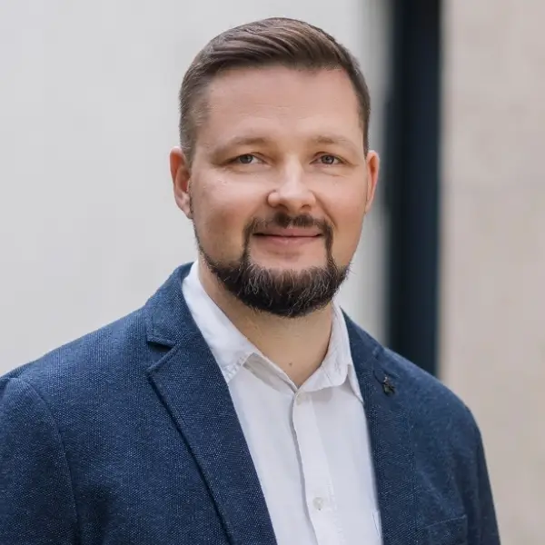 Steuerfachangestellter Anatolii Sirenko in blauem Jackett und weißem Hemd vor heller Hauswand.