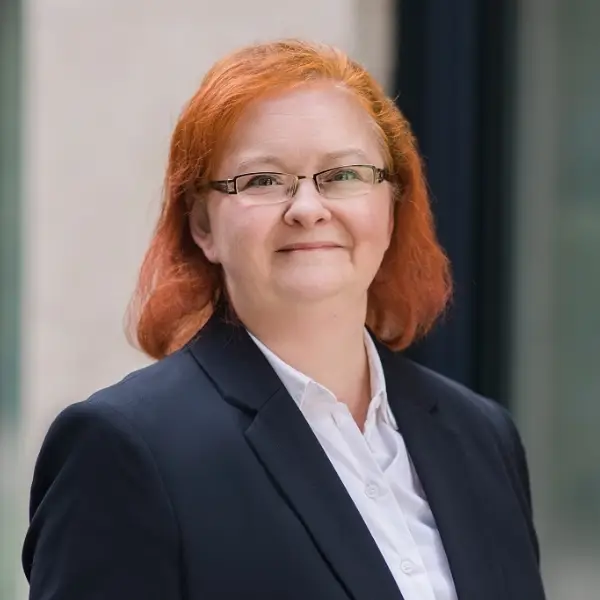 Steuerfachangestellte Anja Meyer in blauem Blazer, weißer Bluse vor heller Hauswand.