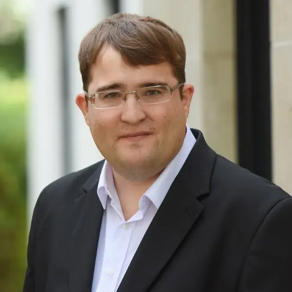 Steuerfachangestellter Axel Bolik in blauem Jackett und weißem Hemd vor heller Hauswand.