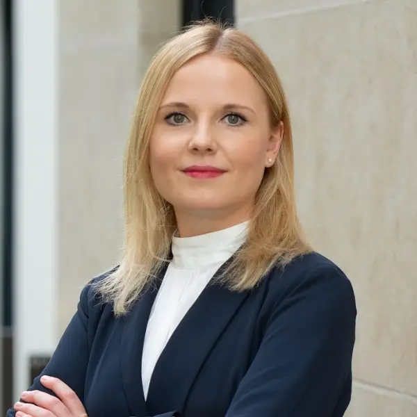 Assistentin der Geschäftsleitung Kathrin Dallmeir in blauem Blazer und weißem Shirt vor heller Hauswand.