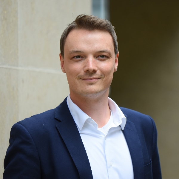 Steuerberater Matthias Mauerer in blauem Jackett und weißem Hemd vor heller Hauswand.