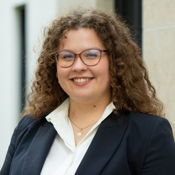 Steuerfachangestellte Viktoria Glavan in blauem Blazer und weißer Bluse vor heller Häuserwand.