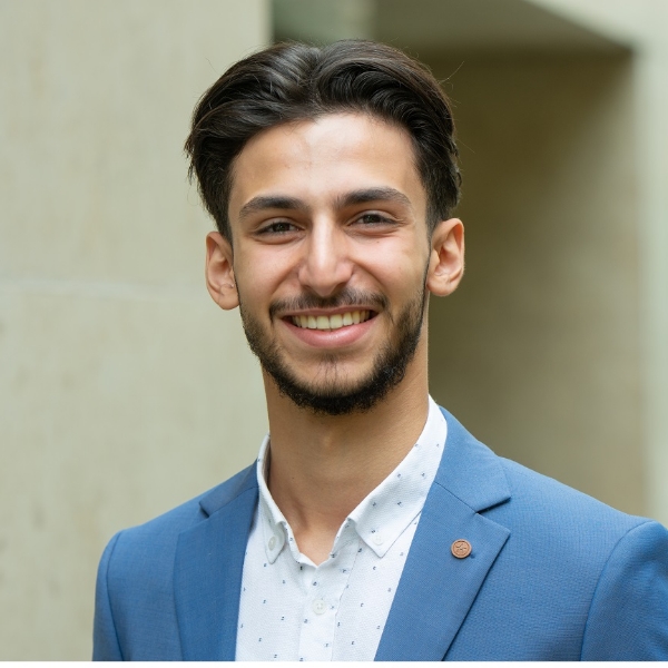 Yasin Aslan in hellblauer Anzugjacke und weißem Hemd vor heller Hauswand.